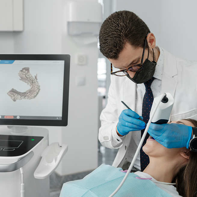 Dentist with glasses taking digital impressions of patient's teeth