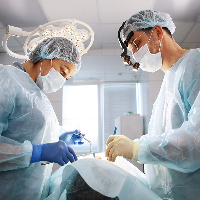 Two dentists on either side of patient performing treatment