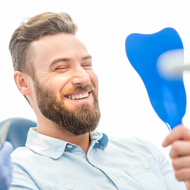 Bearded man smiling and looking in handheld mirror